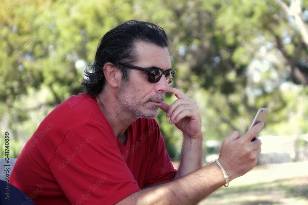 Outdoor portrait of a mid adult man sitting on park bench using mobil phone in Florida, USA Outdoor portrait of a mid adult man sitting on park bench using mobil phone in Florida, USA