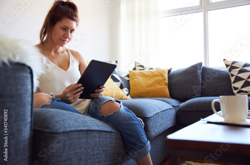 Young female working on tablet computer sat on sofa