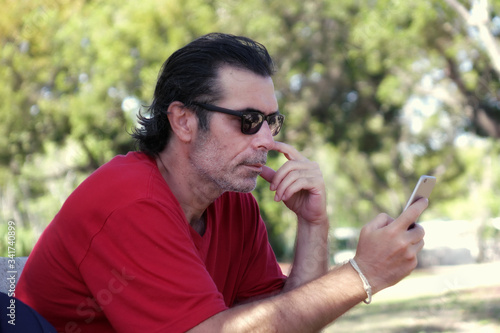 Outdoor portrait of a mid adult man sitting on park bench using mobil phone in Florida, USA