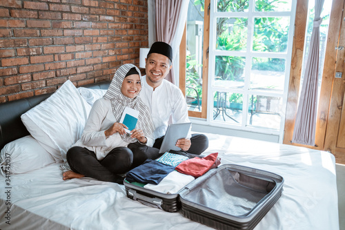 happy portrait of young muslim couple holding passport and tablet packing for holiday