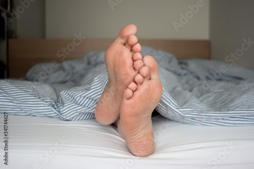 Vászonkép Caucasian male feet sole sticking out from the quilt in bed shallow depth of fie