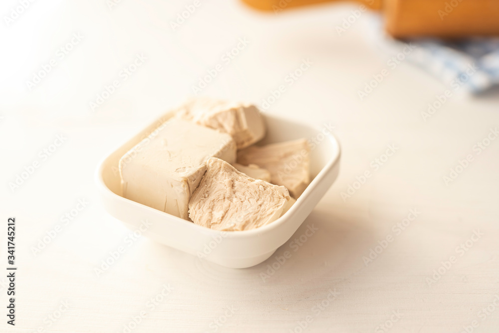 Fototapeta premium close up detail of fresh yeast cube on a white background in a white porcelain dish 
