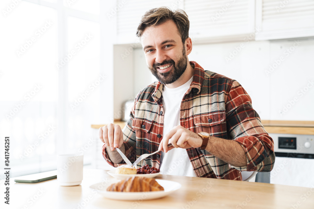 Portrait of joyful man smiling and eating cake while having breakfast Portrait of joyful man smiling and eating cake while having breakfast