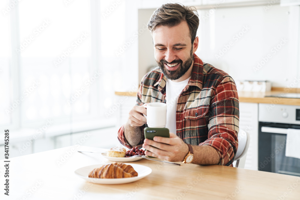 Portrait of smiling bearded man using cellphone and drinking coffee Portrait of smiling bearded man using cellphone and drinking coffee