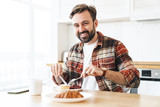 Portrait of joyful man smiling and eating cake while having breakfast