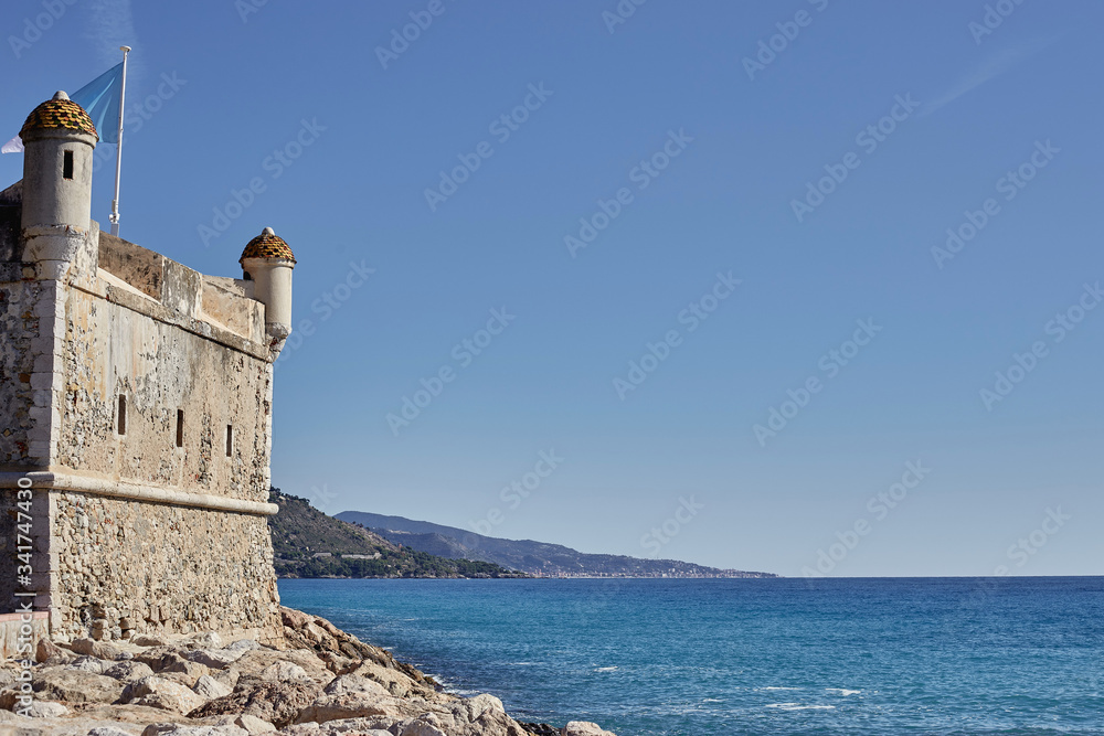 A large stone castle on the shore of the calm sea blue.