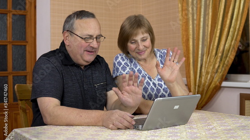 A man and a woman communicate with friends via video communication through a laptop. An old man and an old woman communicate and wave their hands while looking into a laptop. The family is sitting in photo