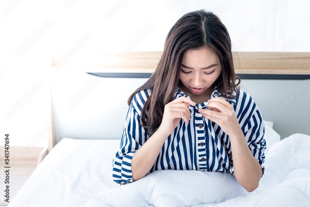 An Asian woman sitting on the white bed, She open her shirt and bent