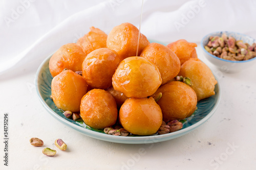 lokma arabic sweet dessert with pistachios in a plate on a white background.