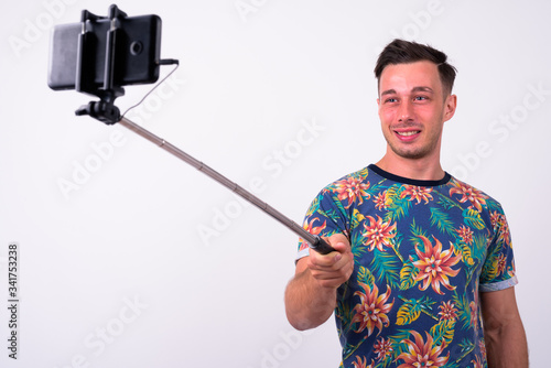 Portrait of happy young tourist man taking selfie with phone on selfie stick
