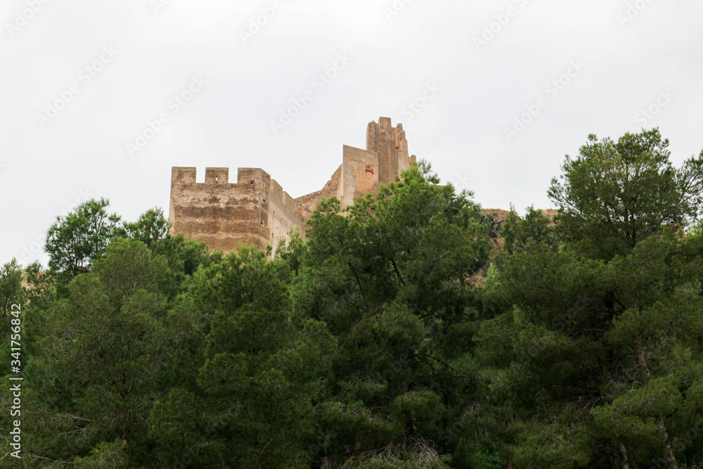 Wall and tower of old medieval Sagunto fortress on a hill in Spain surrounded by green forest