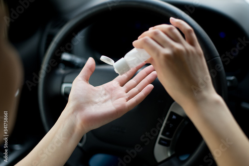 Girl dripping an antiseptic on hand against the background of the steering wheel
