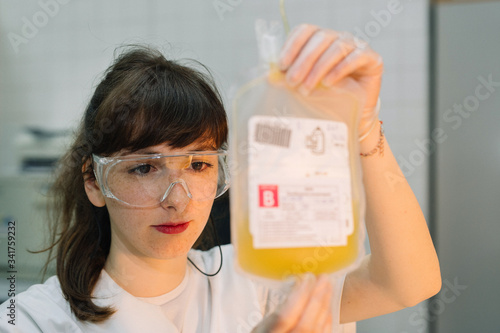 A nurse examines a plastic bag with blood plasma