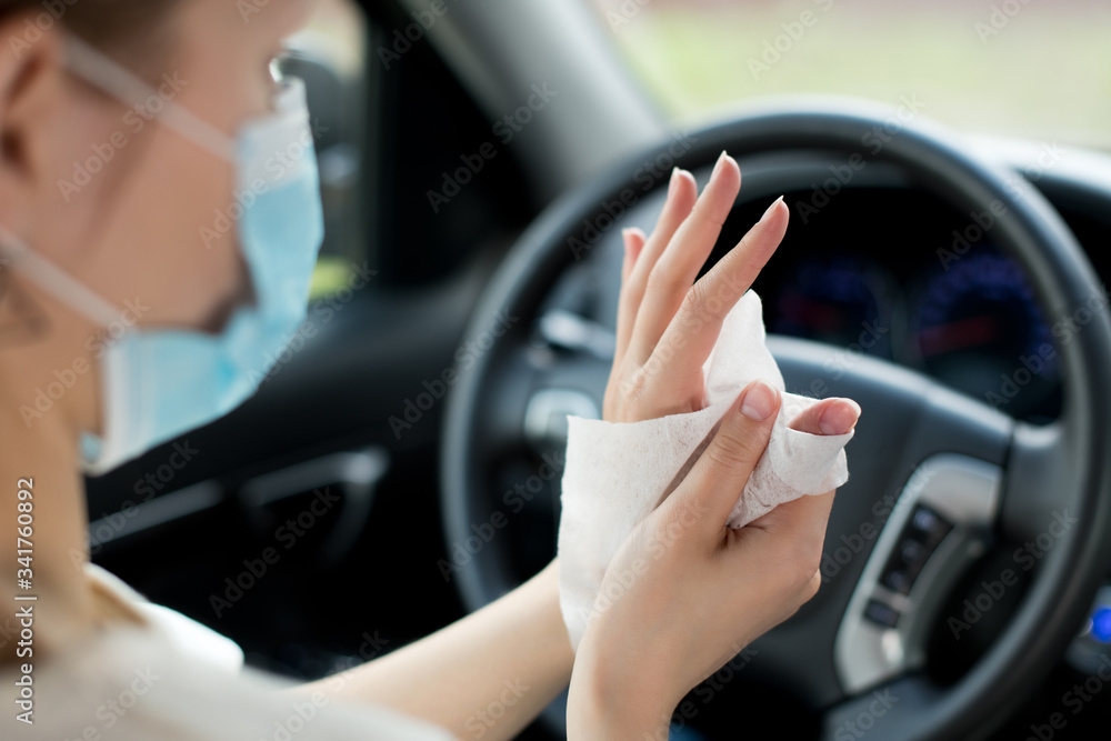 girl in a medical mask rubs her hands with an antiseptic wipe in a car