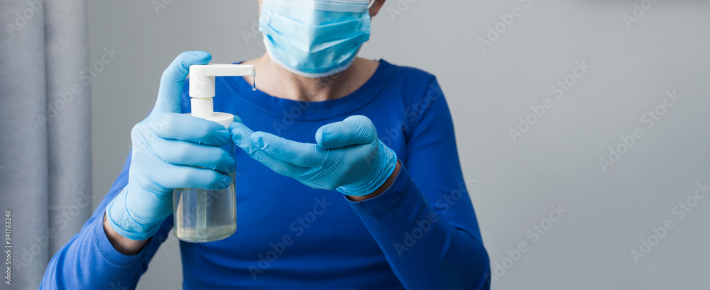 Hand sanitizer bottle in gloved hand closeup. Call for hand disinfection. Stop coronavirus concept banner. Respiratory face mask on background. Using antibacterial gel for hands during quarantine Hand sanitizer bottle in gloved hand closeup. Call for hand disinfection. Stop coronavirus concept banner. Respiratory face mask on background. Using antibacterial gel for hands during quarantine