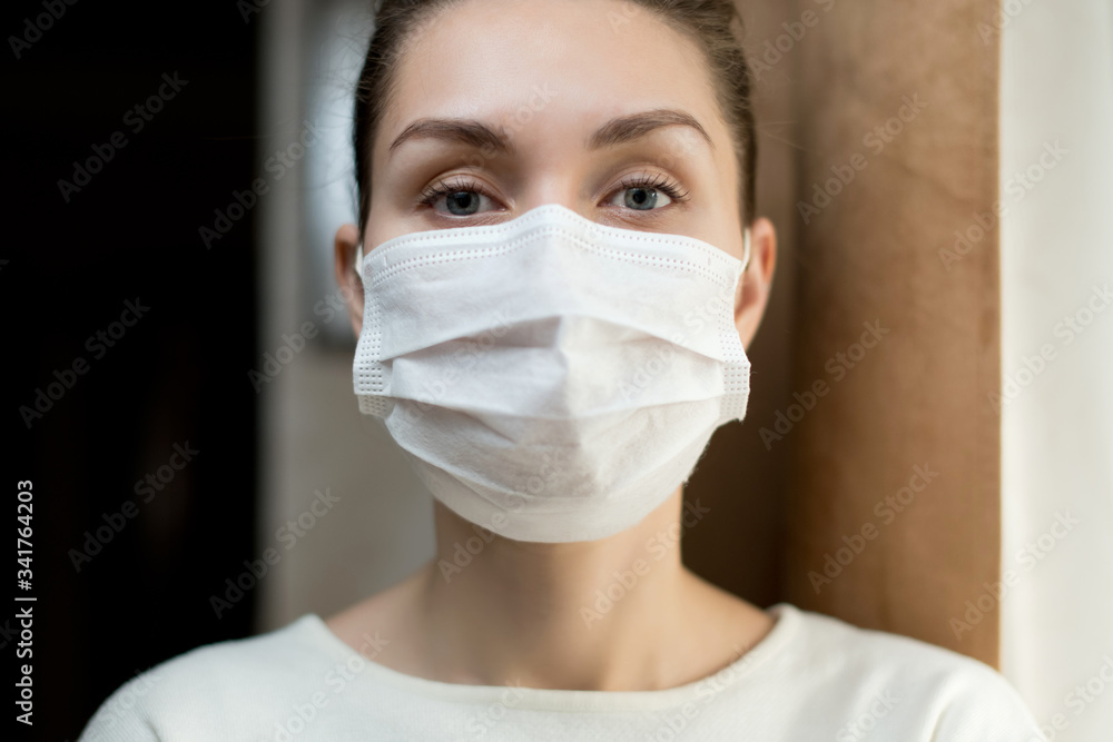 portrait of a girl in a protective medical mask near the window at home portrait of a girl in a protective medical mask near the window at home