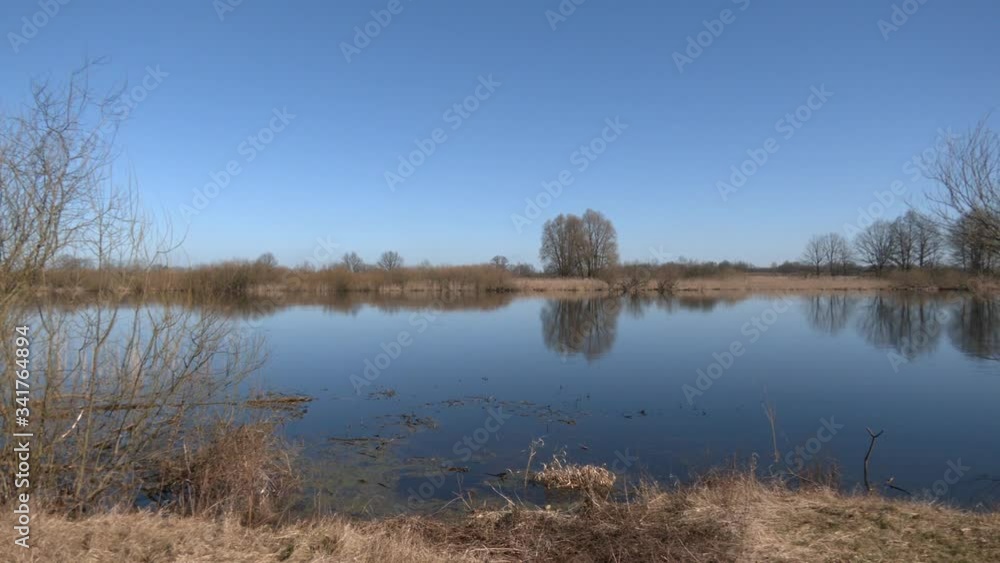 Riverside. Spring. Waves on the water. Dry last year's grass in the light of the sun on the wind. Dry reed on the blue water surface of the river. River in early spring and shore with dry grass.
Riverside. Spring. Waves on the water. Dry last year's grass in the light of the sun on the wind. Dry reed on the blue water surface of the river. River in early spring and shore with dry grass.
