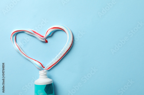 Fototapeta Naklejka Na Ścianę i Meble -  Heart made of toothpaste and tube on blue background, top view