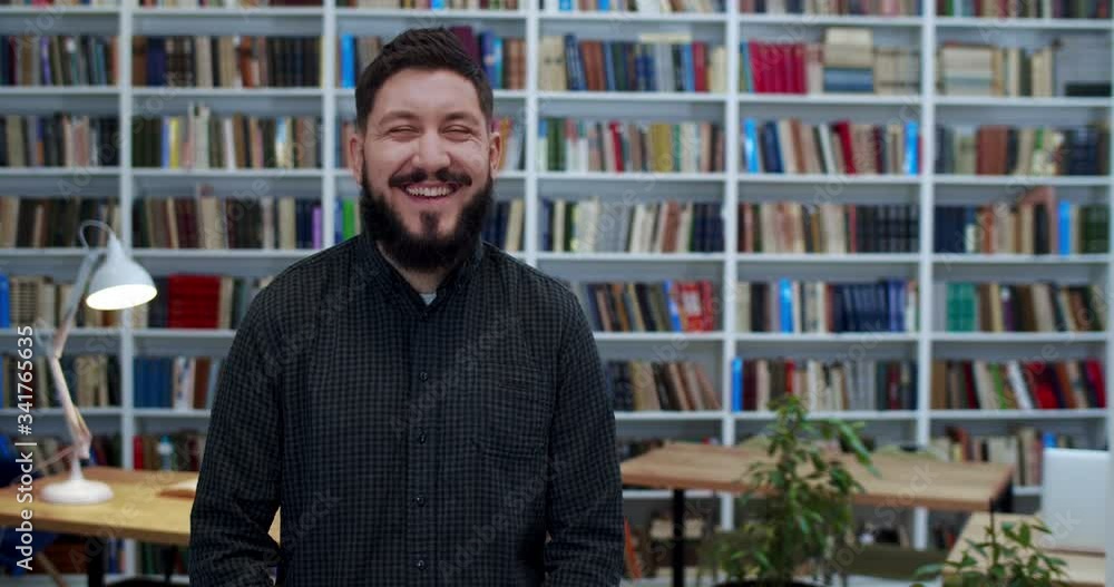 Portrait of cheerful Caucasian man looking to camera and smiling in library. Male customer or joyful worker laughing in bibliotheca. Books shelves on background. Senior smiled teacher. Portrait of cheerful Caucasian man looking to camera and smiling in library. Male customer or joyful worker laughing in bibliotheca. Books shelves on background. Senior smiled teacher.