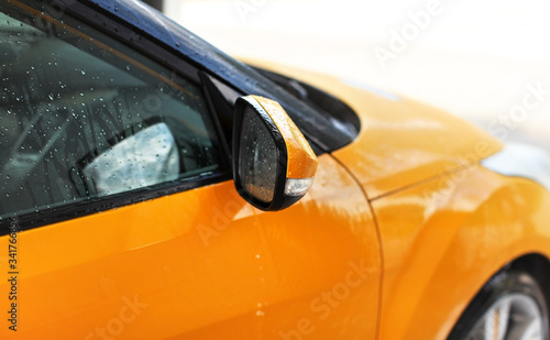 Yellow orange car washed in self serve carwash, detail on side mirror with drops of water