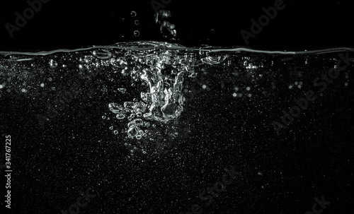 Water pouring into aquarium, black background, detail on dropped liquid creating white bubbles and abstract shapes