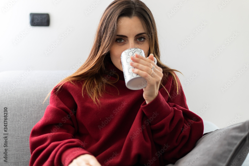 Young woman having a hot drink witting on her sofa Young woman having a hot drink witting on her sofa