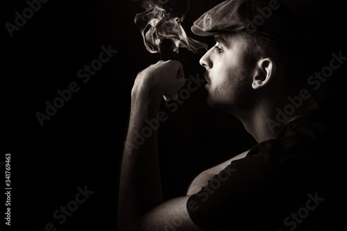 Cute young guy with moustache and a hat on black background smoking a cigarette.