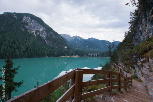 Dirt path to staircase runs along the Braies Lake under a cloudy sky