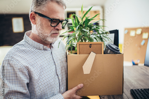 Losing job. Sad quiet man looking frustrated while coming home with a heavy box full of personal items after losing his job. photo