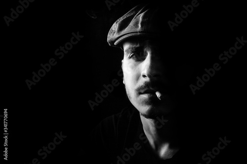 Guy with moustache and a hat on black, dark background smoking a cigarette.
