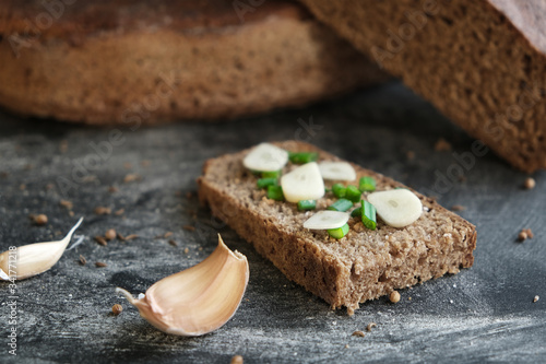 close-up sandwich of piece fresh bread with onion chives and cuts cloves garlic, loaf rye sourdough bread on background