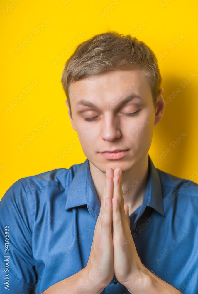 Blond young man folded his hands in prayer to God. Prayer gesture. Close portrait. Isolated yellow background. photo Blond young man folded his hands in prayer to God. Prayer gesture. Close portrait. Isolated yellow background. photo
