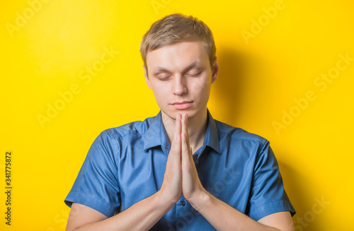 Portrait of handsome young man praying or thinking isolated on yelllow photo