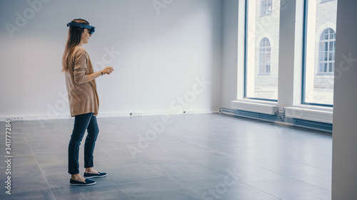 Young Hipster Woman in Holographic Augmented Reality Glasses Standing in Empty Office and Map it. Sunlight Shines Through Big Windows. photo