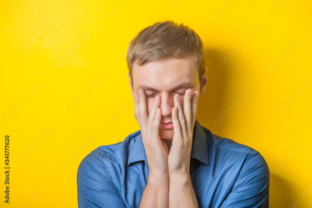 Blond young man thinks thinks. head resting on her hand, looking into the camera. Gesture. Isolated yellow background. Blond young man thinks thinks. head resting on her hand, looking into the camera. Gesture. Isolated yellow background.