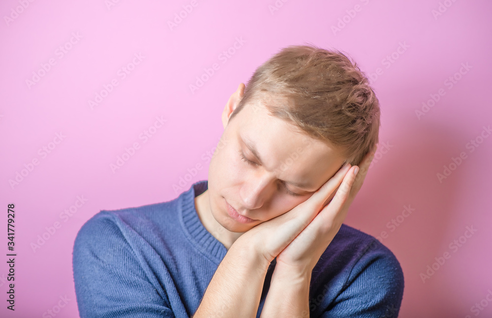 Young Man wants to sleep. Put his head in his hands. Gesture. On a purple background. Young Man wants to sleep. Put his head in his hands. Gesture. On a purple background.