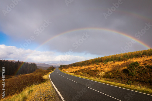 Autumn landscape in Highlands, Scotland, United Kingdom. Road with beautiful and colourful rainbow in background.