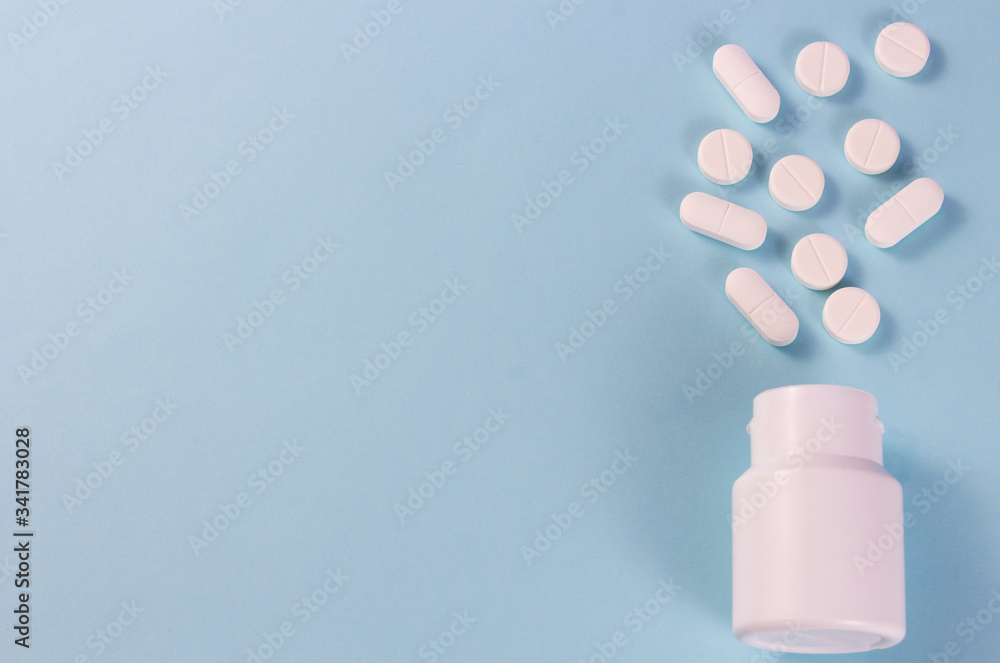 A pile of pills on a blue background. White pills fall out from a white jar on a blue background.copyspace for text. A pile of pills on a blue background. White pills fall out from a white jar on a blue background.copyspace for text.