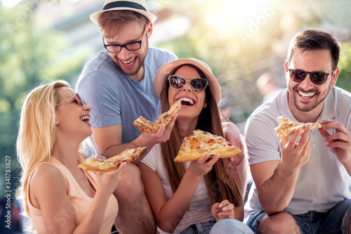 Group of friends eat pizza outdoors.