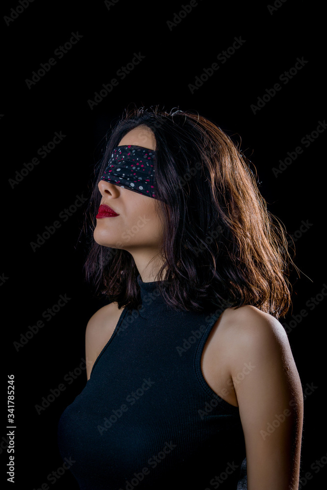 Portrait of beautiful young woman tying her eyes with black scarf on black background Portrait of beautiful young woman tying her eyes with black scarf on black background