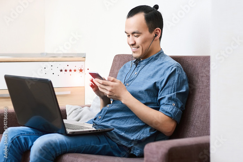 A young smiling Asian guy is holding a smartphone with an icon of a five-star feedback rating. The guy gives an excellent rating for business service services