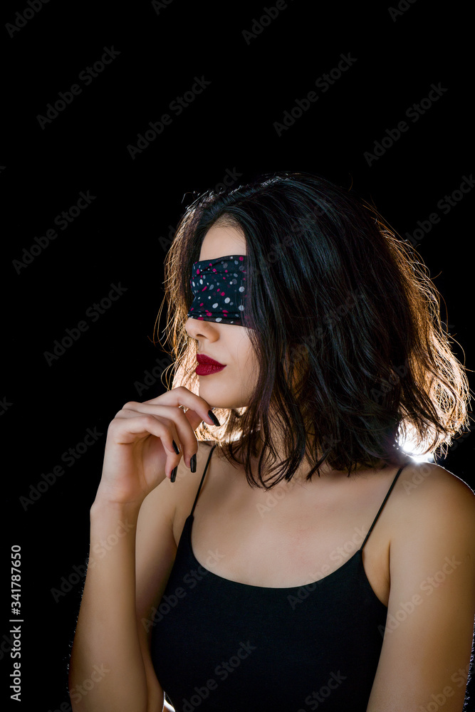 Portrait of beautiful young woman tying her eyes with black scarf on black background Portrait of beautiful young woman tying her eyes with black scarf on black background