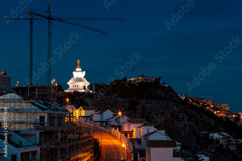 New residential building and a Buddhist white monument with a golden peak at night.  Benalmadena, Malaga / Spain