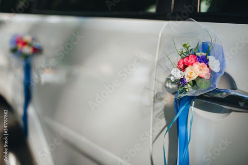 A wedding bouquet of artificial flowers with a ribbon attached to the door of a white car close-up. Photography, concept.