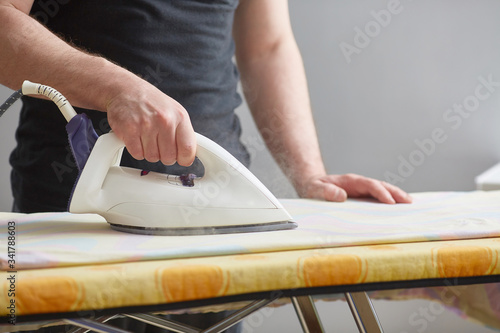 Men's hands hold a white iron and iron on the ironing board. Close-up. Faceless. Copy space. Domestic duties are performed by men.