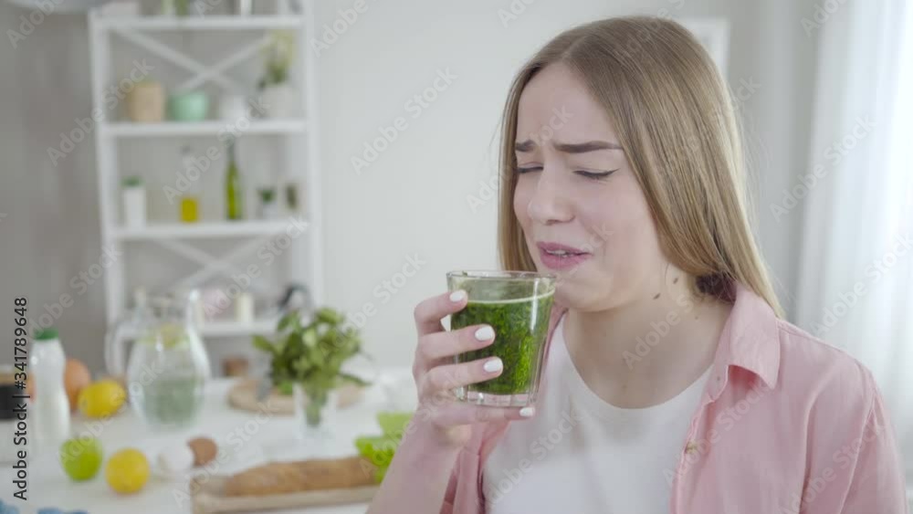 Portrait of unhappy young Caucasian woman drinking herbal detox cocktail. Girl with pucker face dieting indoors. Weight control, self-discipline, health care, healthy lifestyle. Portrait of unhappy young Caucasian woman drinking herbal detox cocktail. Girl with pucker face dieting indoors. Weight control, self-discipline, health care, healthy lifestyle.
