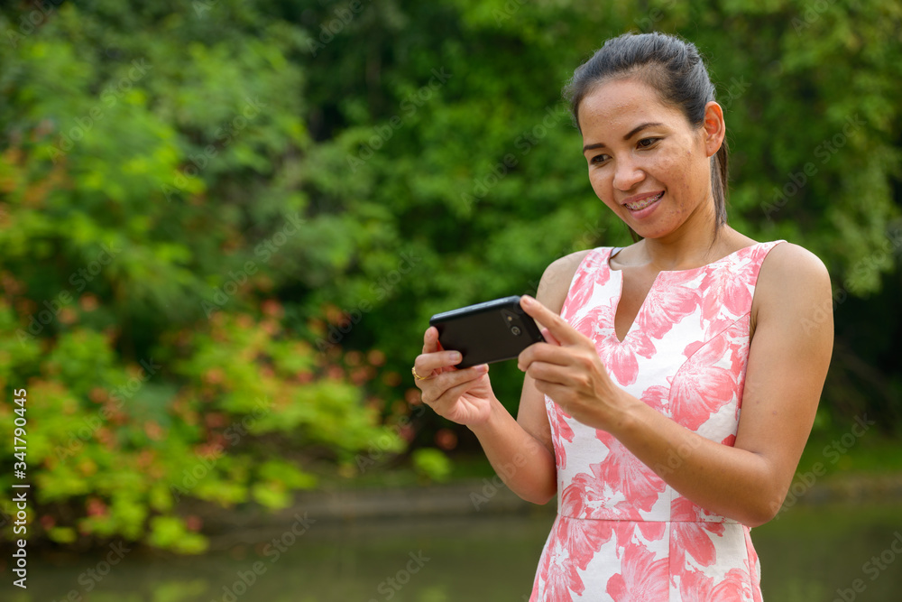 Happy mature Asian woman using phone at the park outdoors Happy mature Asian woman using phone at the park outdoors