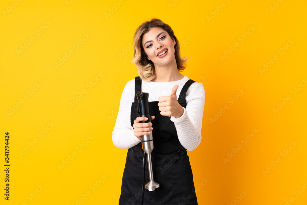 Girl using hand blender isolated on yellow background with thumbs up because something good has happened Girl using hand blender isolated on yellow background with thumbs up because something good has happened