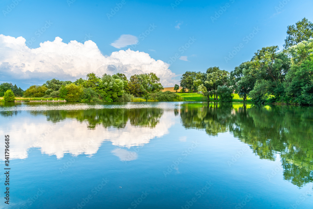 Rural summer landscape reflected in the pond. Blue sky, white clouds and lush green trees Rural summer landscape reflected in the pond. Blue sky, white clouds and lush green trees
