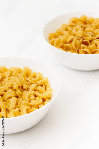 Two different types of unkooked pasta in white bowls isolated